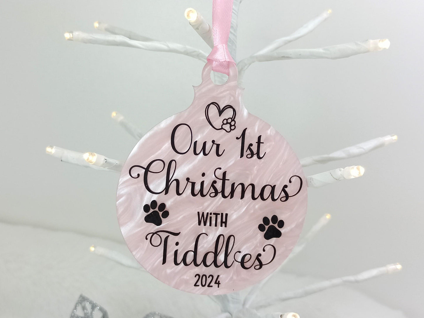 Decorative ornament with 'Our 1st Christmas with Cat or Dog' personalised text on a pink background, hanging against a white Christmas tree.